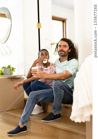 Young diverse couple sitting on stairs at home, enjoying coffee and relaxing together Young diverse couple sitting on stairs at home, enjoying coffee and relaxing together 135677168