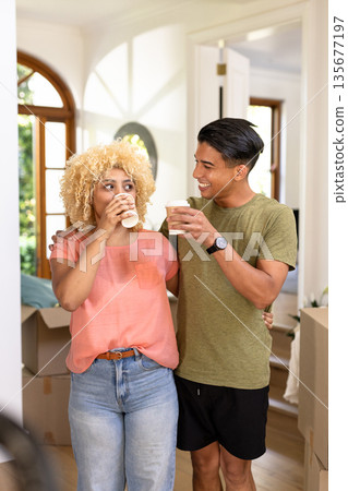 Young diverse couple enjoying coffee break while unpacking boxes in new home Young diverse couple enjoying coffee break while unpacking boxes in new home 135677197