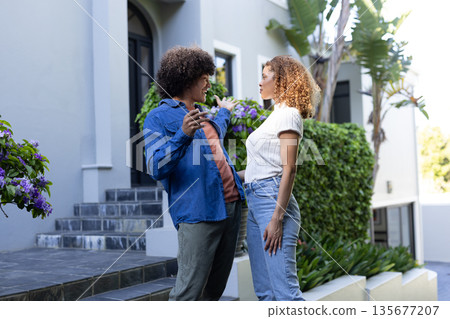 Young couple standing outside modern home, smiling and enjoying conversation Young couple standing outside modern home, smiling and enjoying conversation 135677207