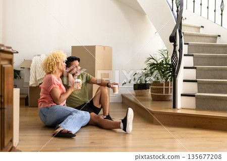 Young couple sitting on floor, enjoying coffee, surrounded by moving boxes at home Young couple sitting on floor, enjoying coffee, surrounded by moving boxes at home 135677208