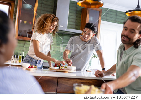 In kitchen, friends sharing snacks and laughter, having conversation together In kitchen, friends sharing snacks and laughter, having conversation together 135677227