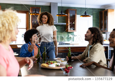 Friends sharing laughter and stories around kitchen table with drinks and conversation 135677229