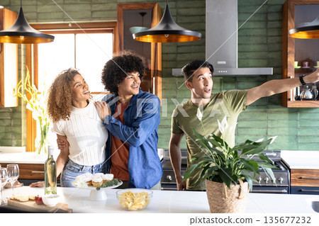 Friends laughing and pointing while enjoying time together in modern kitchen Friends laughing and pointing while enjoying time together in modern kitchen 135677232