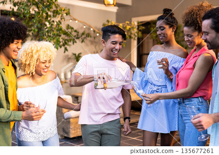 Young Diverse friends enjoying outdoor party, smiling and pouring drinks together Young Diverse friends enjoying outdoor party, smiling and pouring drinks together 135677261