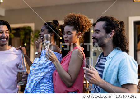 Young Diverse friends enjoying drinks and laughing together at outdoor gathering 135677262