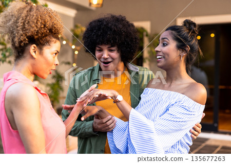 Celebrating engagement, Diverse friends admiring ring with excitement at outdoor gathering 135677263