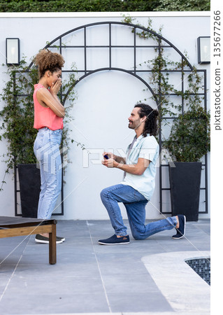 Man proposing to surprised woman outdoors, holding engagement ring, joyful moment Man proposing to surprised woman outdoors, holding engagement ring, joyful moment 135677266