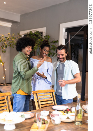 Diverse friends enjoying casual gathering with drinks and snacks at home, smiling together 135677268