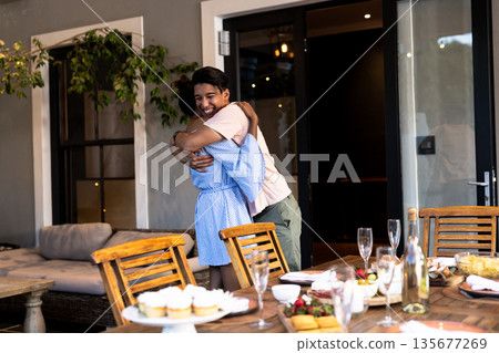 Diverse friends hugging joyfully at outdoor gathering with cupcakes and champagne on table 135677269