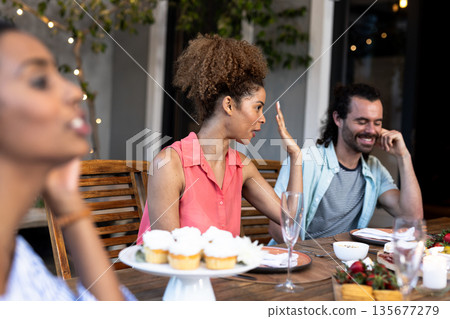 Diverse friends enjoying outdoor dinner party with cupcakes and lively conversation Diverse friends enjoying outdoor dinner party with cupcakes and lively conversation 135677279