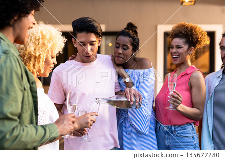 Young Diverse friends enjoying outdoor gathering, pouring champagne and laughing together Young Diverse friends enjoying outdoor gathering, pouring champagne and laughing together 135677280