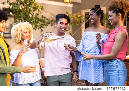 Young Diverse friends celebrating outdoors, pouring champagne and enjoying festive gathering 135677282