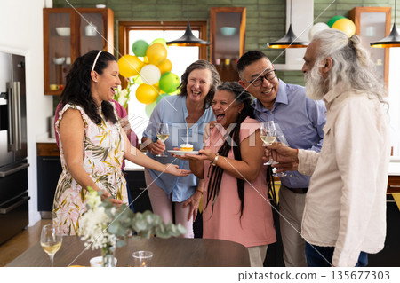 Celebrating birthday at home, diverse seniors laughing and drinking wine together Celebrating birthday at home, diverse seniors laughing and drinking wine together 135677303