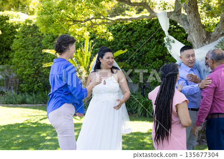 Celebrating in lush garden, bride in white dress joyfully with friends Celebrating in lush garden, bride in white dress joyfully with friends 135677304