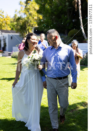 Celebrating senior wedding, bride walking joyfully with father in garden holding bouquet 135677311