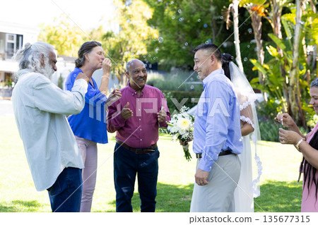 Blowing bubbles at joyful senior wedding party, diverse group celebrating outdoors Blowing bubbles at joyful senior wedding party, diverse group celebrating outdoors 135677315