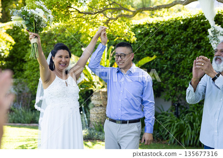 Celebrating senior wedding outdoors, joyful couple holding hands and smiling with guests 135677316