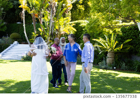 In garden, bride hugging guest while others chatting and smiling nearby In garden, bride hugging guest while others chatting and smiling nearby 135677338