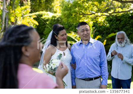 Celebrating outdoors, bride and groom standing together surrounded by friends 135677341