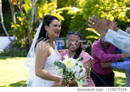 Bride celebrating with friends in garden, holding bouquet and smiling joyfully Bride celebrating with friends in garden, holding bouquet and smiling joyfully 135677356