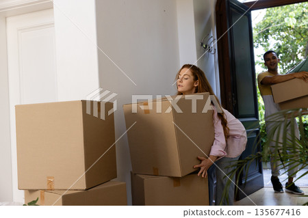 Young couple moving boxes into new home, smiling and enjoying fresh start Young couple moving boxes into new home, smiling and enjoying fresh start 135677416