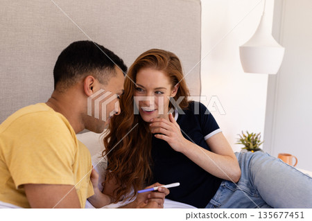 Young couple at home smiling and holding pregnancy test on bed 135677451