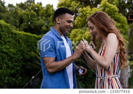 Young man proposing to joyful woman with engagement ring in lush garden Young man proposing to joyful woman with engagement ring in lush garden 135677458