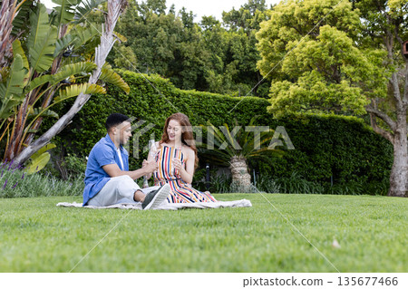 Young couple sitting on grass enjoying drinks and sharing joyful moment 135677466