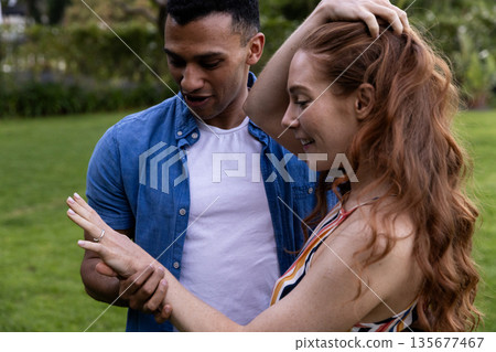 Young couple celebrating engagement in park, admiring ring with joy Young couple celebrating engagement in park, admiring ring with joy 135677467