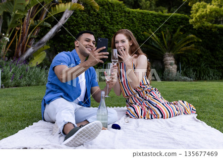 Young couple enjoying picnic in park, taking selfie with smartphone, smiling happily Young couple enjoying picnic in park, taking selfie with smartphone, smiling happily 135677469
