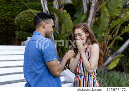 Young couple in garden, man proposing with ring, woman surprised and emotional Young couple in garden, man proposing with ring, woman surprised and emotional 135677472