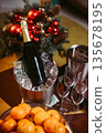 Champagne bottle in an ice bucket with glasses, tangerines in a vase and evergreen branches in background. Elegant New Year festive composition, vertical studio photo. 135678195