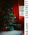 Christmas tree near a window with red curtains. Santa sack and vintage wooden chest under the tree, cozy festive interior, vertical composition. 135678577