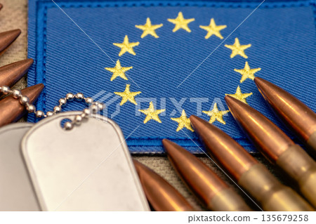 Military ammunition and metal identification tags on blue European Union flag. Military ammunition and metal identification tags on blue European Union flag. 135679258