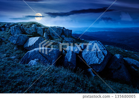 mountain landscape in summer with rocks at night. grass under dark sky in full moon light. alpine meadow and rolling hills with boulders. backdrop for evil fiction art or mystery concepts mountain landscape in summer with rocks at night. grass under dark sky in full moon light. alpine meadow and rolling hills with boulders. backdrop for evil fiction art or mystery concepts 135680005