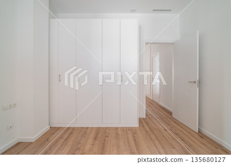 A bright, minimalist interior featuring a white wardrobe and wooden flooring. The walls are plain and the space is uncluttered, emphasizing simplicity and modern design. A bright, minimalist interior featuring a white wardrobe and wooden flooring. The walls are plain and the space is uncluttered, emphasizing simplicity and modern design. 135680127