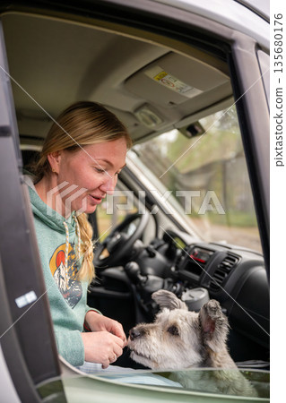 Woman traveling in camper van with dog looking through window enjoying road trip lifestyle 135680176