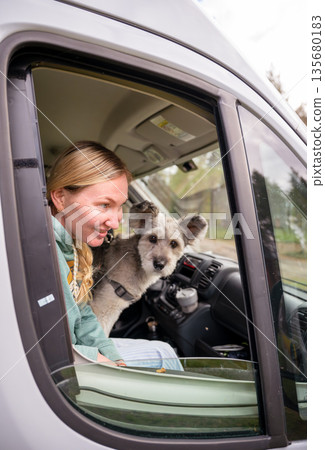 Woman traveling in camper van with dog looking through window enjoying road trip lifestyle Woman traveling in camper van with dog looking through window enjoying road trip lifestyle 135680183