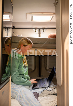 Woman working on laptop inside camper van during travel lifestyle remote work concept Woman working on laptop inside camper van during travel lifestyle remote work concept 135680192