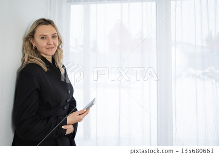 Smiling Blonde Woman in Black Blazer Uses Phone by White Curtains Smiling Blonde Woman in Black Blazer Uses Phone by White Curtains 135680661