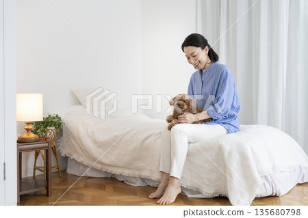 一位中年婦女坐在床上,抱著她的寵物狗 一位中年婦女坐在床上,抱著她的寵物狗 135680798