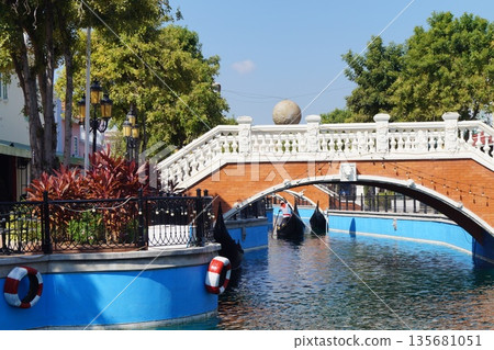 Little Venice in Thailand.Streets and canals of old Venice in Thailand with wooden gondolas, stone bridges, and a blue sky in the background. 135681051