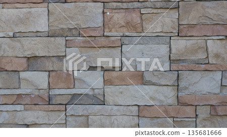 A fragment of a tiled wall made of natural stone, a mosaic of square shapes of different sizes in a gray-brown color scheme, decorative stone finishing tiles in the design of exterior surfaces 135681666