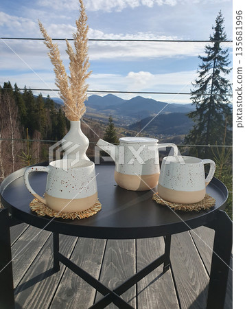 Two cups of tea on a coffee pot on a small table on a terrace with a view of the Carpathian Mountains. Two cups of tea on a coffee pot on a small table on a terrace with a view of the Carpathian Mountains. 135681996