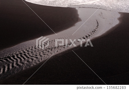 A gentle stream of water on a black sand beach A gentle stream of water on a black sand beach 135682283
