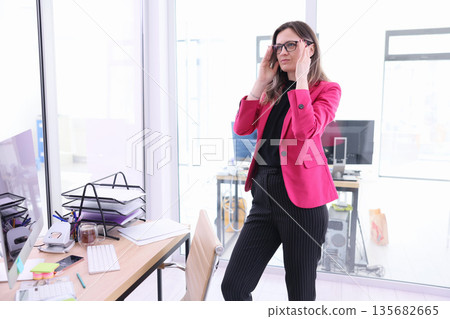 Focused professional adjusts glasses in a bright office space while planning her next move with determination and style 135682665
