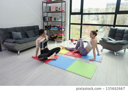 Friends practicing yoga together in a bright and cozy room filled with colorful mats 135682667