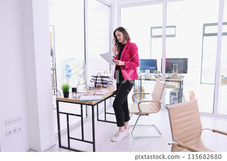 Professional woman reviewing documents in a modern office space during a busy workday, capturing productivity and focus 135682680