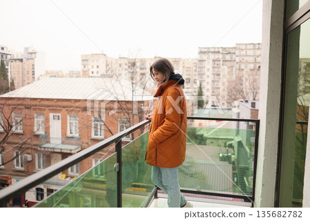Young woman enjoys a quiet moment on the balcony with city views during a cloudy afternoon Young woman enjoys a quiet moment on the balcony with city views during a cloudy afternoon 135682782