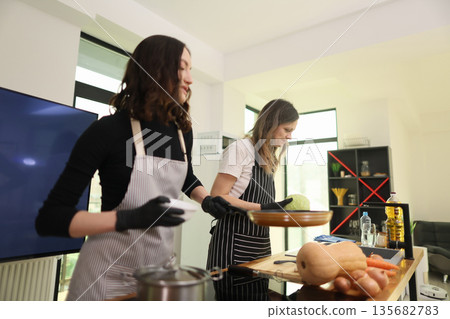 Cooking enthusiasts prepare a delicious meal together in a modern kitchen during a sunny afternoon Cooking enthusiasts prepare a delicious meal together in a modern kitchen during a sunny afternoon 135682783